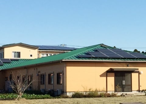 緑色の屋根と太陽光パネルを備えた介護施設の外観。温かみのあるベージュ色の壁面が特徴。