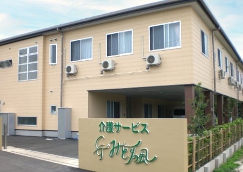 介護施設の建物外観。クリーム色の2階建て施設で、玄関前に看板がある。
